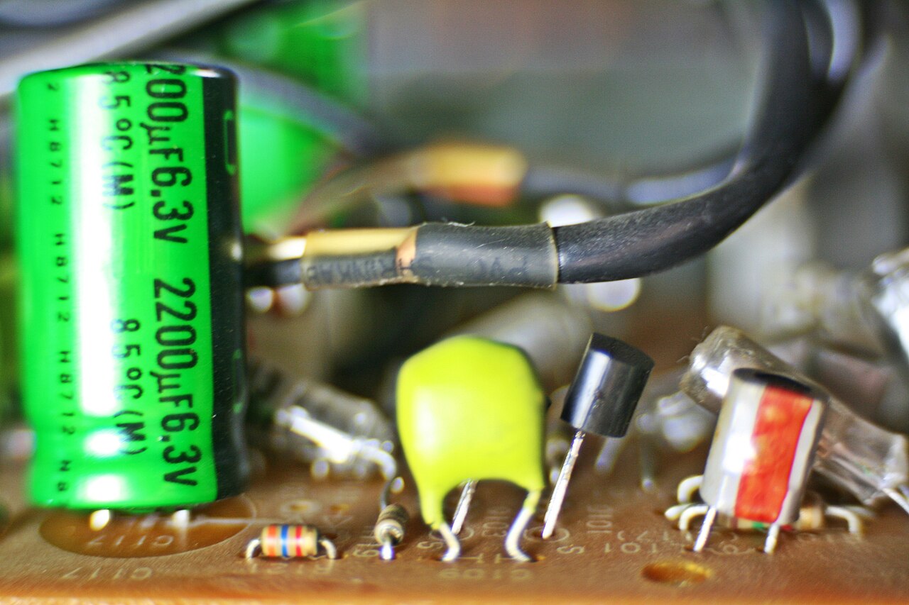 A macro photograph of a circuit board showing a large green capacitor and fine copper traces